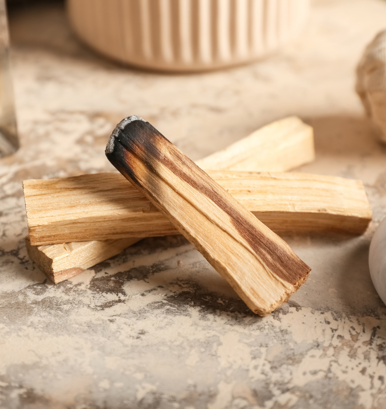 Burnt wood next to marble, colonge, and a ramekin as a visual representation of Palo Santo Fragrance Oil available at Village Craft and Candle || Bois brûlé à côté du marbre, d'une colonge et d'un ramequin comme représentation visuelle de l'huile parfumée Palo Santo disponible chez Village Craft and Candle