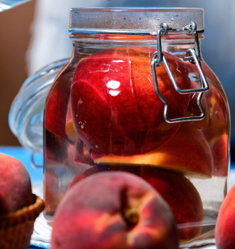 Peaches preserved in a jar with a metal clasp as a visual representation of Orchard Peach Preserve Fragrance Oil available at Village Craft and Candle || Pêches conservées dans un pot avec un fermoir en métal comme représentation visuelle de l'huile parfumée Orchard Peach Preserve disponible chez Village Craft and Candle