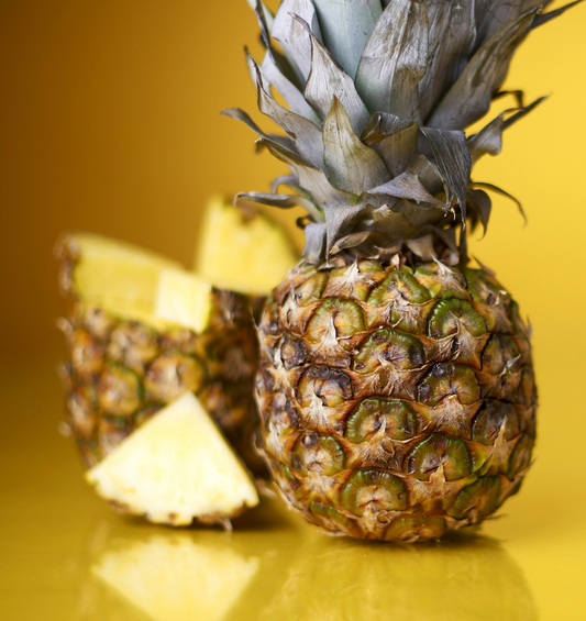  Tranches d'ananas avec un ananas entier en arrière-plan comme représentation visuelle de l'huile parfumée d'ananas disponible chez Village Craft and Candle.
