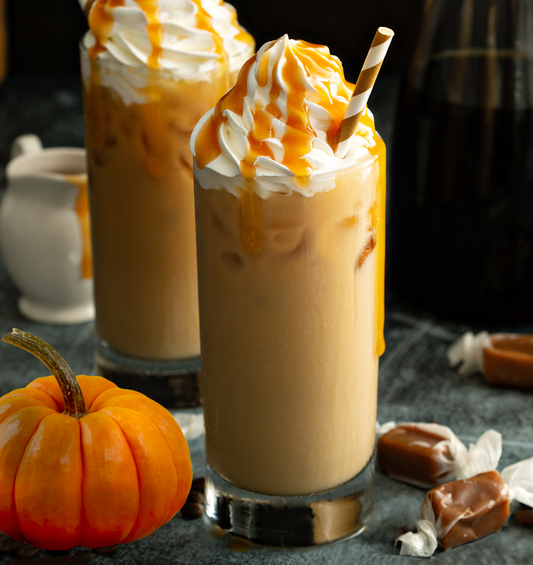 Two iced pumpkin caramel lattes with caramel and pumpkins surrounding them as a visual representation of Pumpkin Caramel Fragrance Oil available at Village Craft and Candle 