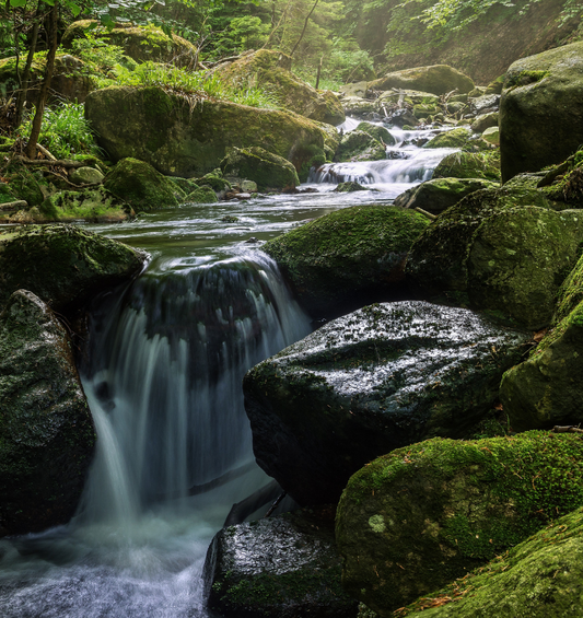  Cascade coulant sur des rochers moussus comme représentation visuelle de l'huile parfumée River Stone disponible chez Village Craft and Candle