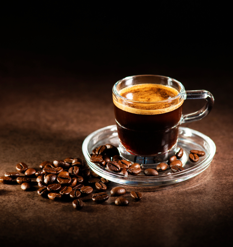 Glass of espresso surrounded by coffee beans on glass tray as a visual representation of Roasted Espresso Fragrance Oil available at Village Craft and Candle || Verre d'espresso entouré de grains de café sur un plateau en verre comme représentation visuelle de l'huile parfumée d'espresso torréfié disponible chez Village Craft and Candle