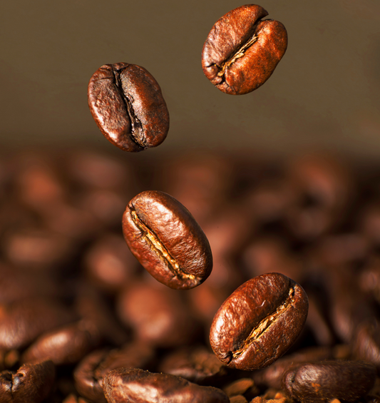 A few coffee beans dropping into pile of roasted beans as a visual representation of Roasted Java Fragrance Oil available at Village Craft and Candle 