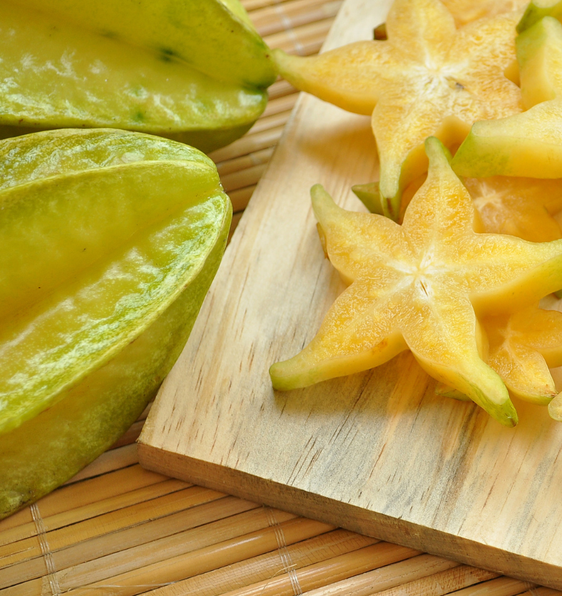 Sliced starfruit on a cutting board as a visual representation of Starfruit & Aloe Fragrance Oil available at Village Craft and Candle || Carambole tranchée sur un lit de feuilles de palmier comme représentation visuelle de l'huile parfumée de carambole et d'aloès disponible chez Village Craft and Candle.