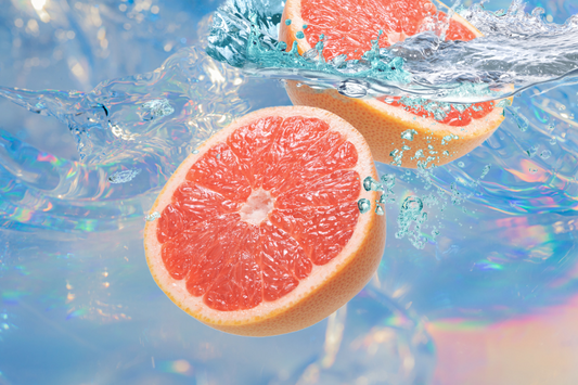Grapefruits underneath a blue and pink shimmering pool as a visual representation of Uplifting Essential Oil Blend available at Village Craft and Candle 