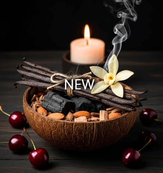 Vanilla Emberwood Fragrance Oil represented by vanilla beans, almonds, wood, and charcoal in a bowl with cherries and a lit candle, evoking a smoky vanilla aroma. 