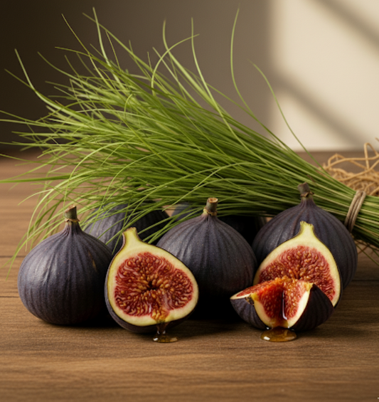 Close-up still life of whole and halved ripe purple figs with honey-like liquid dripping from them, positioned next to a bundle of tall, green vetiver grass on a wooden surface. 