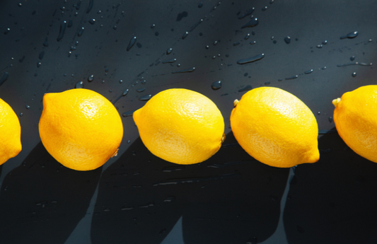 Quatre citrons sur une table noire humide comme représentation visuelle de l'huile parfumée au citron propre disponible chez Village Craft and Candle