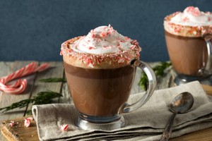 Frothy mochaccino coffee in a glass mug topped with whipped cream and crushed candy cane pieces || Café mochaccino mousseux dans une tasse en verre garnie de crème fouettée et de morceaux de canne en bonbon écrasés