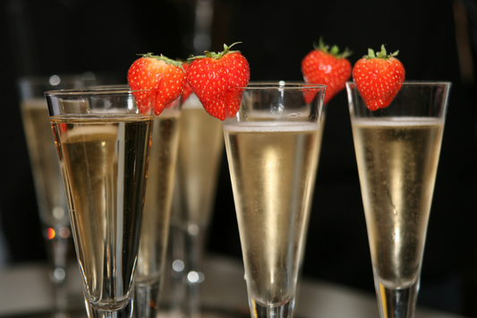  Flûtes Campange avec des fraises sur les lèvres des verres comme représentation visuelle de l'huile parfumée aux fraises et au champagne disponible chez Village Craft and Candle