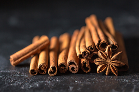 Cinnamon sticks and a cinnamon clove on black table as a visual representation of Ceylon Cinnamon Leaf Essential Oil available at Village Craft and Candle 