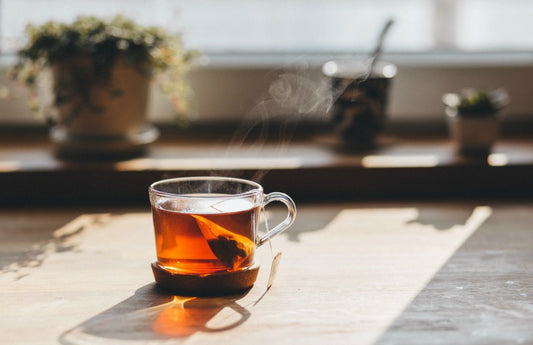Steaming glass of early gray tea in the sunlight with potted plants in the background as a visual representation of Earl Grey Tea Fragrance Oil available at Village Craft and Candle 