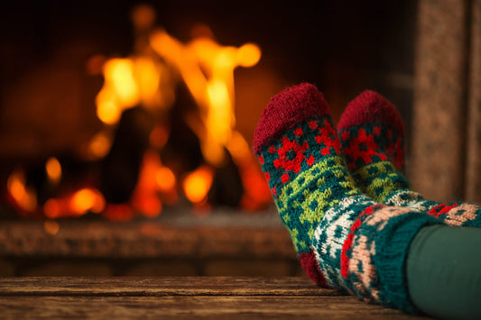  Chaussettes de Noël sur pieds à côté d'une cheminée comme représentation visuelle de l'huile parfumée au coin du feu disponible chez Village Craft and Candle