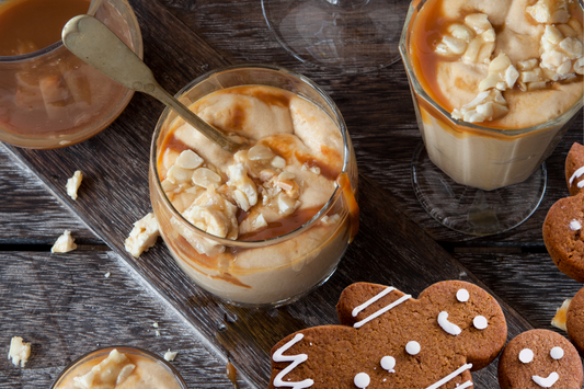 Creamy mousse dessert with carmel sauce topping in a glass sitting beside gingerbread with white icing 