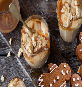 Creamy mousse dessert with carmel sauce topping in a glass sitting beside gingerbread with white icing ||  Dessert mousse crémeuse avec garniture de sauce au caramel dans un verre assis à côté de pain d'épice avec glaçage blanc