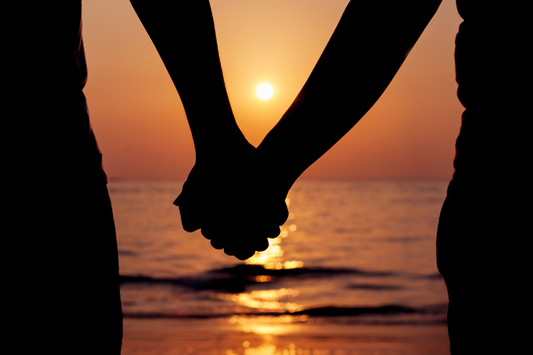 Couple se tenant la main devant un coucher de soleil sur l'océan comme représentation visuelle de l'huile parfumée Love Spell disponible chez Village Craft and Candle