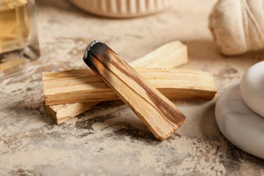 Burnt wood next to marble, colonge, and a ramekin as a visual representation of Palo Santo Fragrance Oil available at Village Craft and Candle 