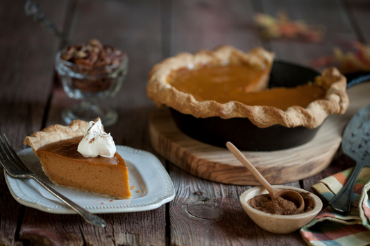 A slice of garnished pumpkin pie with spices and the full pie in the background as a visual representation of Pumpkin Pie Fragrance Oil available at Village Craft and Candle 