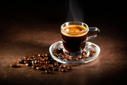  Verre d'espresso entouré de grains de café sur un plateau en verre comme représentation visuelle de l'huile parfumée d'espresso torréfié disponible chez Village Craft and Candle