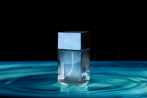 Glass cologne bottle in center of puddle of rippling blue water || Bouteille d'eau de Cologne en verre au centre d'une flaque d'eau bleue ondulante
