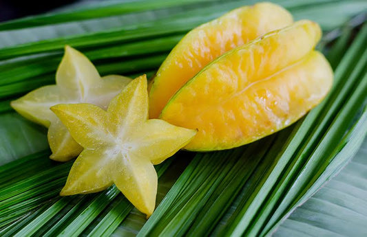 Sliced starfruit on a bed of palm leaves as a visual representation of Starfruit & Aloe Fragrance Oil available at Village Craft and Candle 