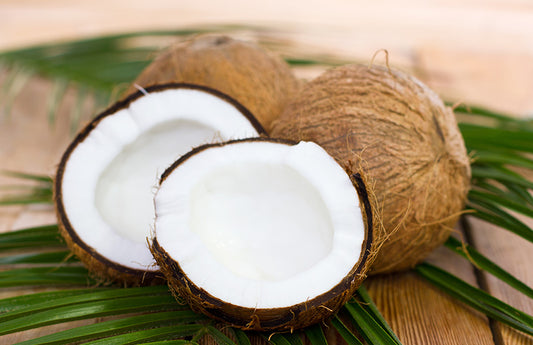  Casser des noix de coco sur des feuilles de palmier comme représentation visuelle de l'huile parfumée à la noix de coco disponible chez Village Craft and Candle.
