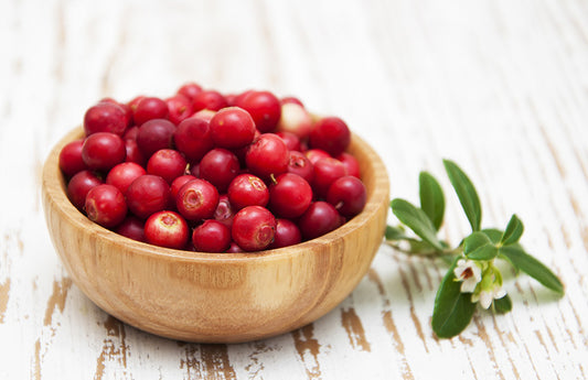 Wood bowl of cranberries atop a birch table as a visual representation of Cranberry Fragrance Oil available at Village Craft and Candle 