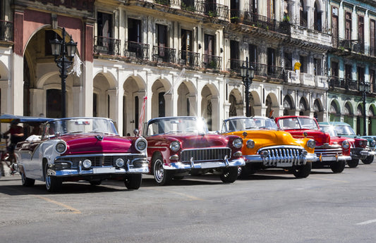  Voitures classiques de différentes couleurs devant de vieux bâtiments cubains comme représentation visuelle de l'huile parfumée de La Havane disponible chez Village Craft and Candle