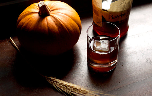  Verre de bourbon à côté de citrouille et de blé comme représentation visuelle de l'huile parfumée de citrouille bourbon disponible chez Village Craft and Candle