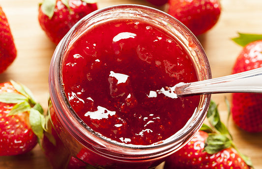 Close up of strawberry jam with strawberries in the background as a visual representation of Strawberry Jam Fragrance Oil available at Village Craft and Candle 